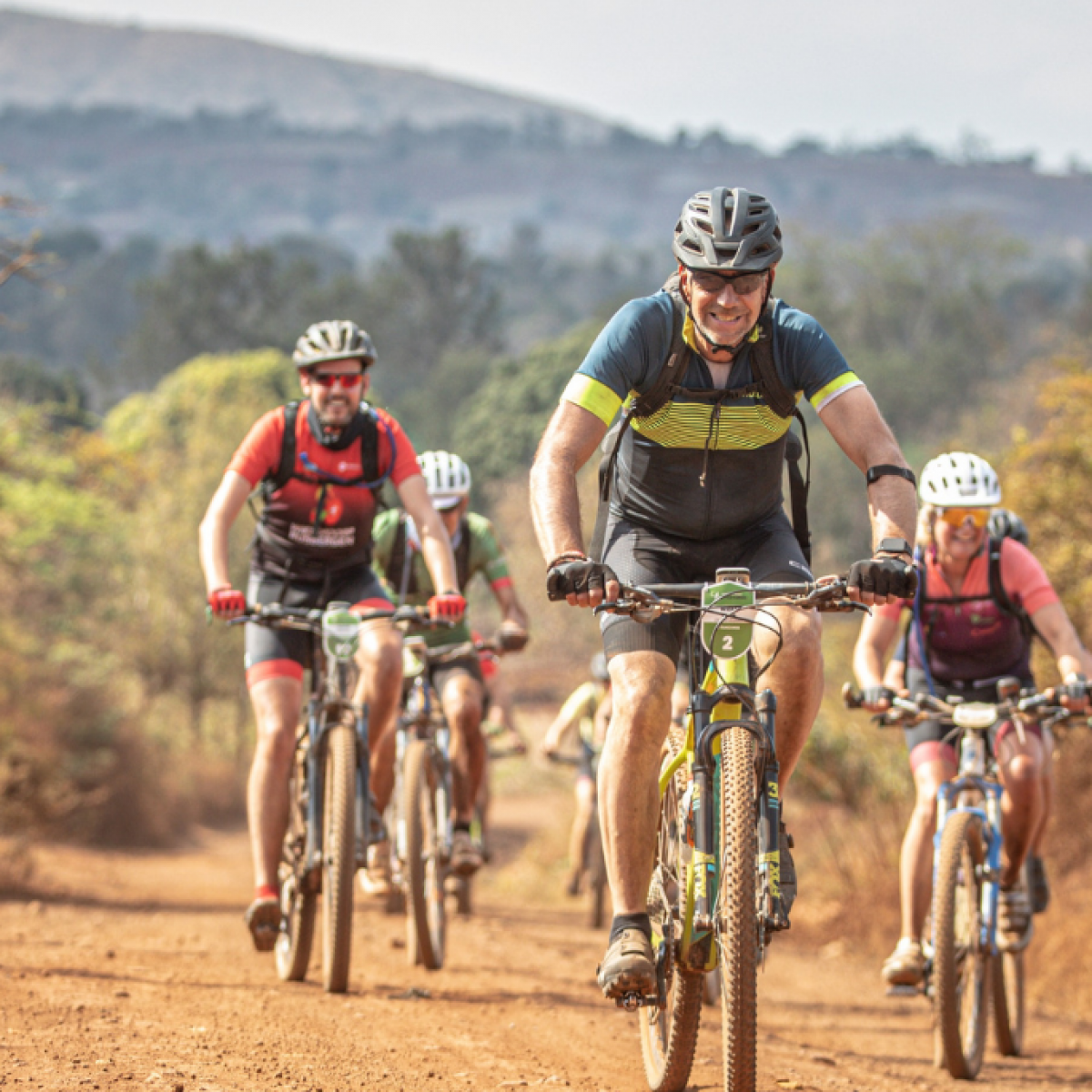 Deelnemers Africa Classic zwaaien naar camera terwijl ze over de savanne fietsen