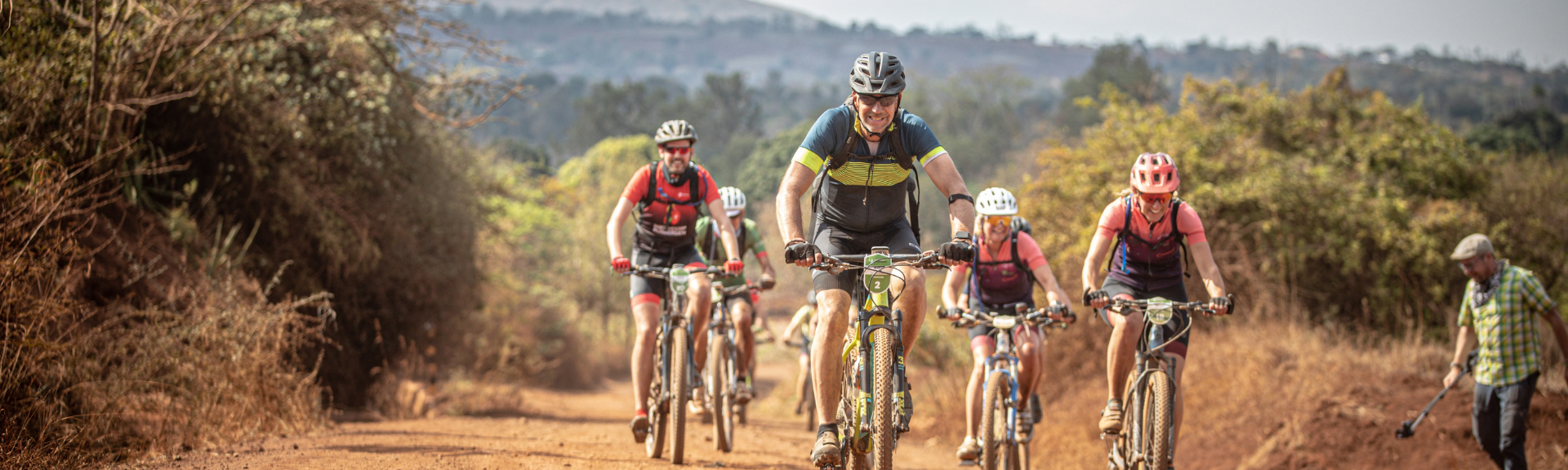 Deelnemers Africa Classic zwaaien naar camera terwijl ze over de savanne fietsen